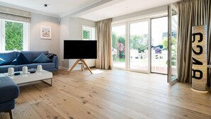 A modern living room with a flat-screen TV, a blue sofa, and a coffee table. - Strandhütte - House Strandhütte (Sylt)