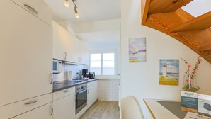 A modern kitchen with white cabinets, stainless steel appliances, and a wooden dining table.