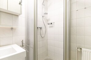 A modern bathroom with a glass-enclosed shower, white tiles, a white sink, and a radiator. - Appartement Wellenreiter (Sylt)
