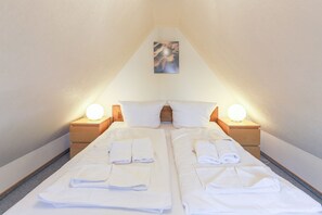 A room with two beds, each with a nightstand and a lamp, and a painting on the wall. - Appartement Wellenreiter (Sylt)