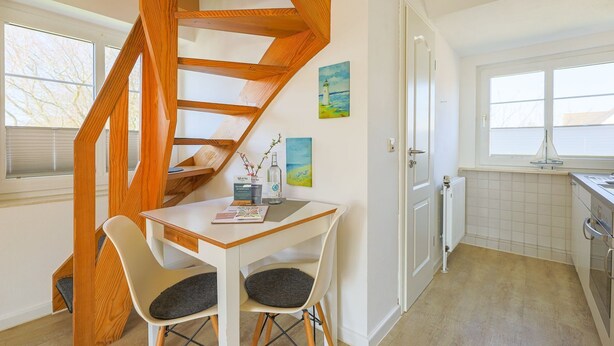 Una cocina moderna con una escalera espiral de madera, un comedor con dos sillas y vistas al exterior a través de una ventana.