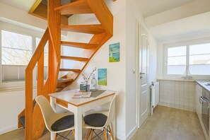 Une cuisine moderne avec un escalier en colimaçon en bois, un coin repas avec deux chaises et une vue sur l’extérieur par une fenêtre.