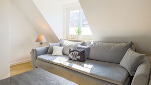 Una sala de estar moderna con un sofá gris, una lámpara y una ventana que ofrece vistas a un edificio.