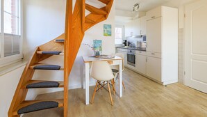 Una cocina moderna con armarios blancos, una mesa de comedor con sillas y una escalera de madera con peldaños acolchados.