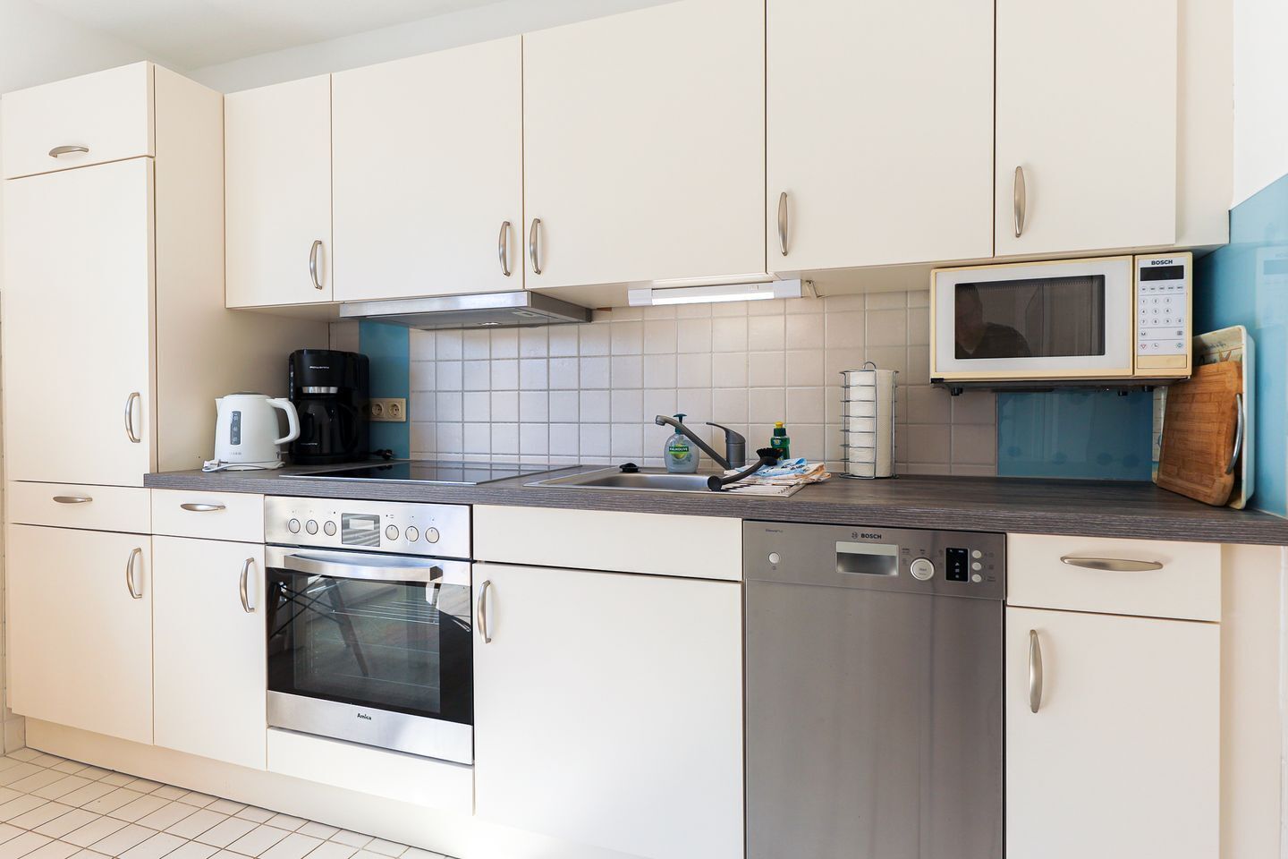 A modern kitchen with white cabinets, a Bosch microwave, a coffee maker, and a dishwasher.