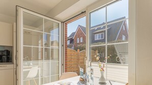 A modern kitchen with a dining area, large windows, and a view of neighboring houses.