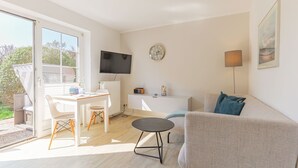 A modern living room with a sofa, a dining table with chairs, a TV mounted on the wall, and a radiator.