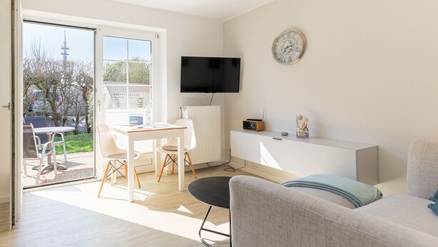 A modern living room with a sofa, a TV, a clock, and a dining area with a table and chairs.