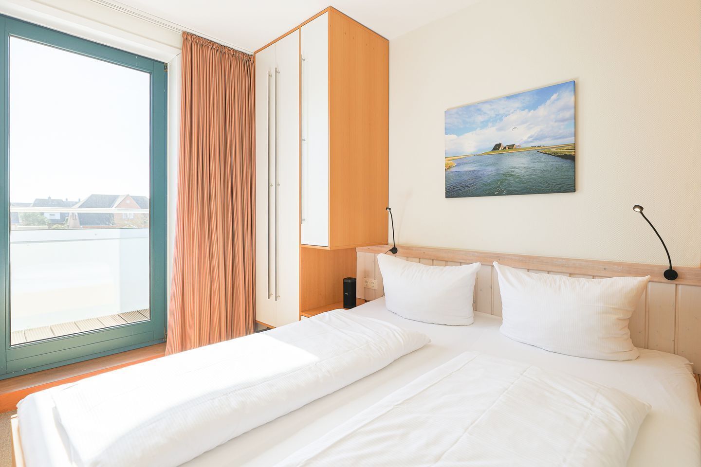Une chambre d’hôtel avec un lit, un tableau représentant un paysage, une fenêtre avec des rideaux et une vue sur les bâtiments à l’extérieur.