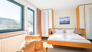 Et hotelværelse med en stor seng, en stol, et skrivebord og udsigt til det fri.