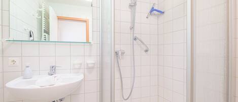 Un baño con un lavamanos blanco, un espejo y una ducha.