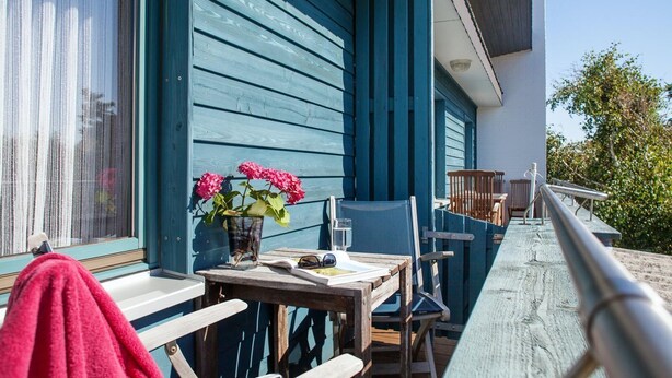 En træterrasse med et bord, stole, en potteplante og et rødt håndklæde.