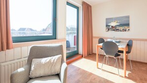 A room with a view of a bridge, a dining area with a table and chairs, and a window with curtains. - Greenlön - House Tilly - Greenlön (Sylt)