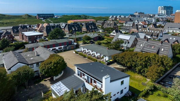 An aerial view of a residential area with houses, a parking lot, and a view of the sea. - Greenlön - House Tilly - Greenlön (Sylt)