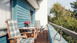 A wooden deck with two tables and four chairs, a small table with a vase of flowers, and a white wall with a window. - Greenlön - House Tilly - Greenlön (Sylt)