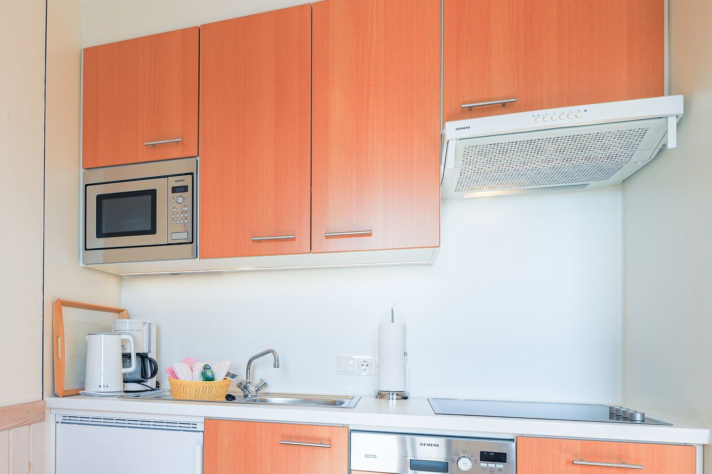 Une cuisine compacte dotée de meubles en bois, d’un four à micro-ondes, d’une machine à café et d’une hotte aspirante Siemens.