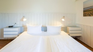 A hotel room with a large bed, two bedside tables, and a wall-mounted lamp. - Greenlön - House Tilly - Greenlön (Sylt)
