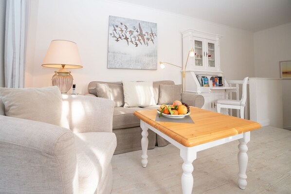 Un salon avec un canapé, une table basse en bois sur laquelle se trouvent des fruits, une lampe et un meuble contenant des livres.
