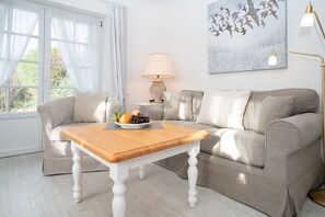 Una sala de estar con una mesa de centro de madera, un sofá color beige, una lámpara y un cuadro en la pared.