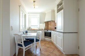 Une cuisine avec des meubles blancs, un fourneau et un coin repas comprenant une table et des chaises.