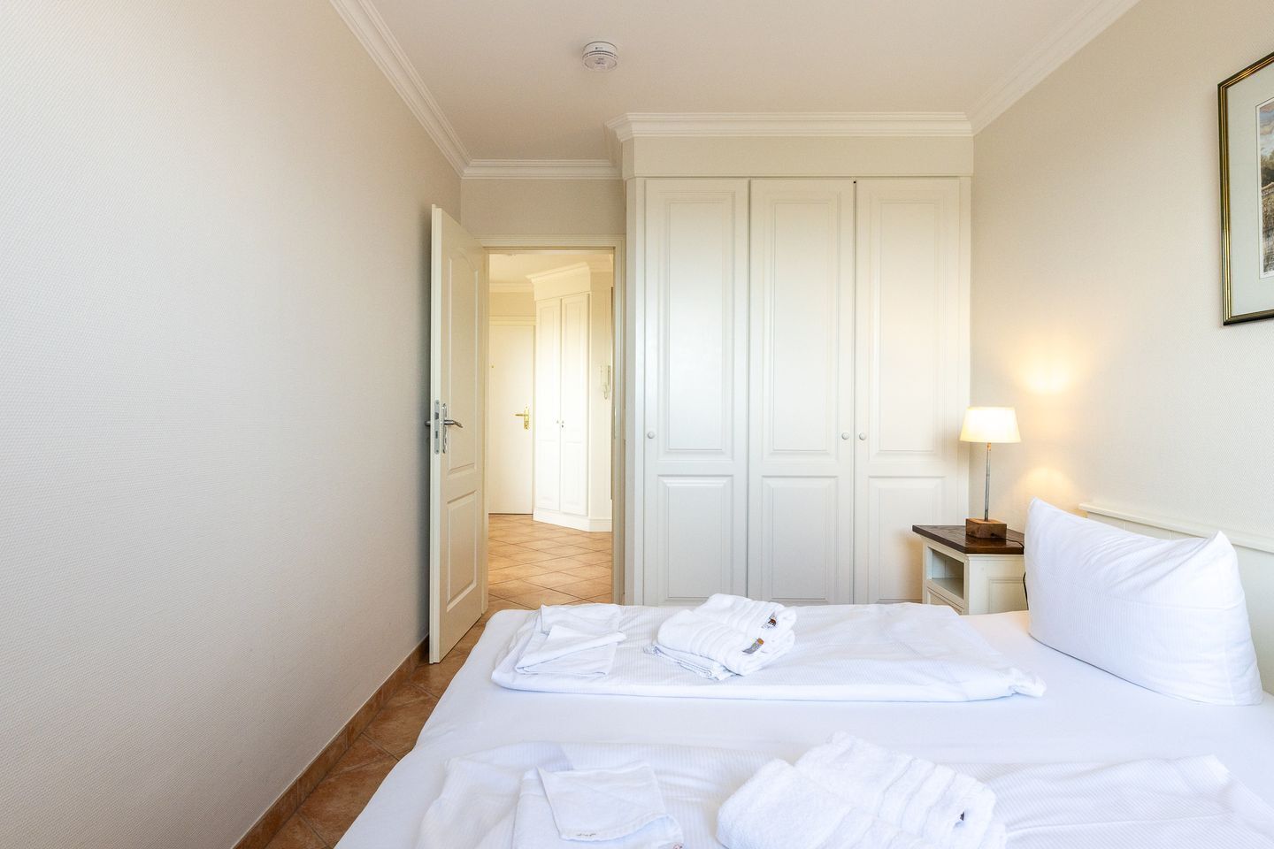 A hotel room with a neatly made bed, a bedside lamp, and a door leading to another room.
