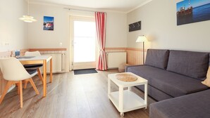 Ein gut beleuchteter Raum mit Esstisch, Stühlen, einer Couch, einem kleinen Beistelltisch und einer Lampe.