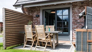 A patio with a wooden table and chairs, a brick wall, and a glass door leading inside.