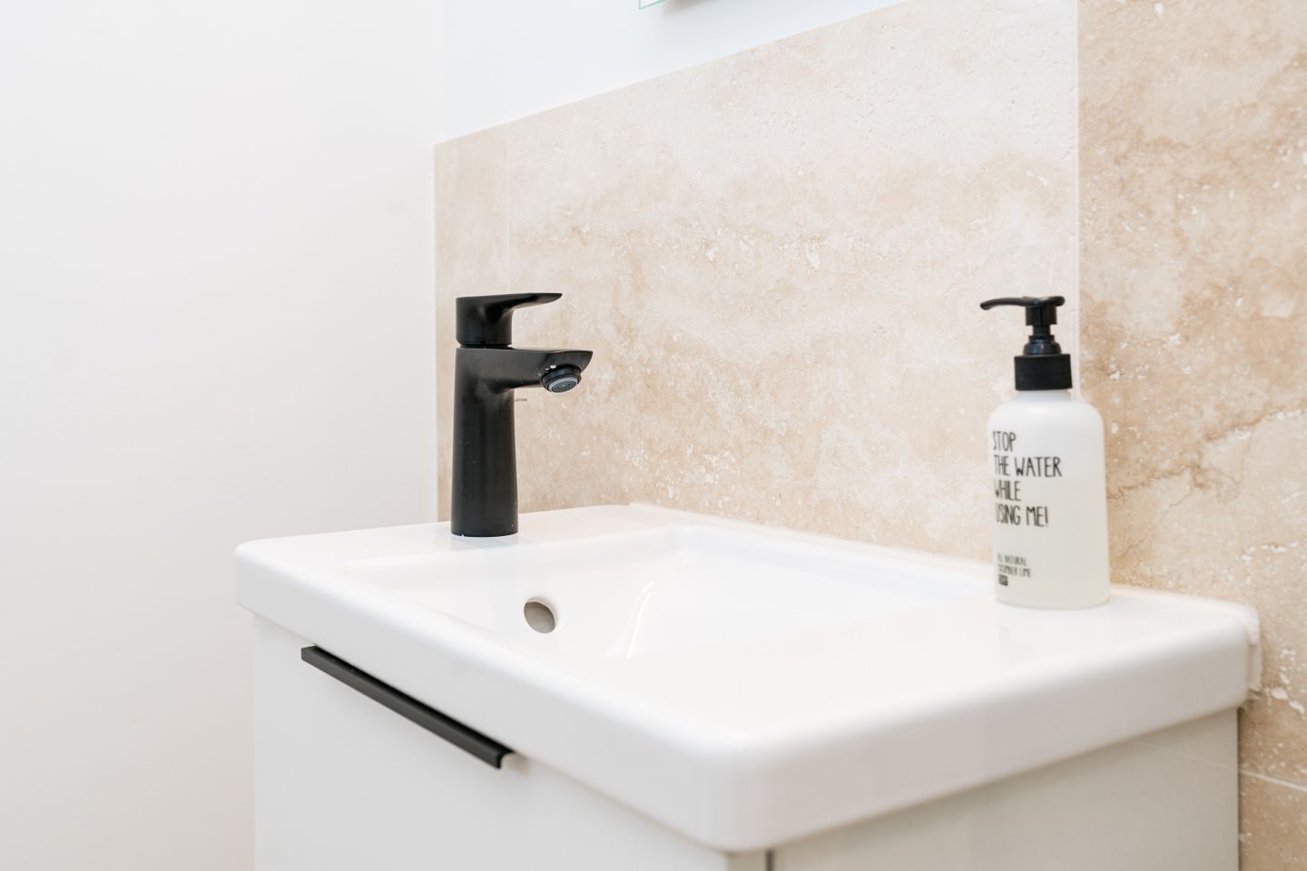 Une salle de bain avec un lavabo blanc, un robinet noir et un flacon de savon pour les mains.
