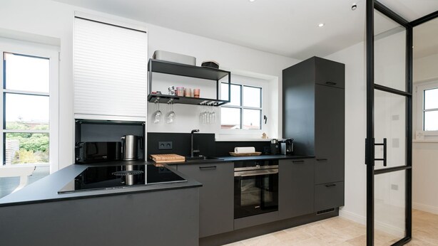 A modern kitchen with a black countertop, stainless steel appliances, and a built-in oven. - Hüs gur seen, Germany (Sylt)