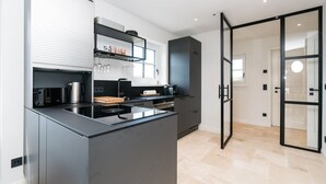 A modern kitchen with a central island, built-in appliances, and a glass door leading to another room.