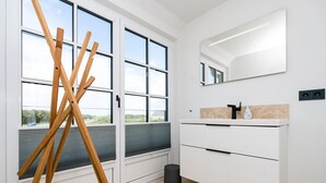 A modern bathroom with a large window, a wooden ladder, a white sink, and a mirror.