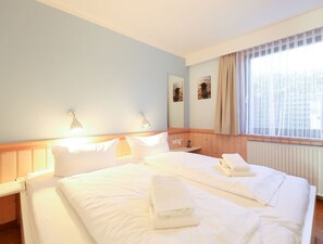 Una habitación de hotel con una cama grande, dos mesitas de noche, un velador, una ventana con cortinas y lámparas fijadas a la pared.