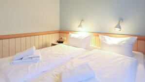 Une chambre d’hôtel avec une tête de lit en bois, deux lampes de chevet, un téléviseur à écran plat et des lits parfaitement faits.