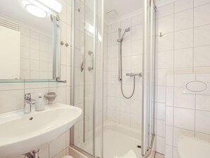 Un baño moderno con ducha acristalada, lavabo blanco y espejo.