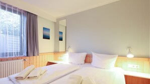 A hotel room with a large bed, two bedside tables, a window with curtains, a radiator, and a wall-mounted mirror.