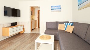 A modern living room with a grey sofa, a flat-screen TV, a wooden cabinet, and a small white table with a woven placemat.