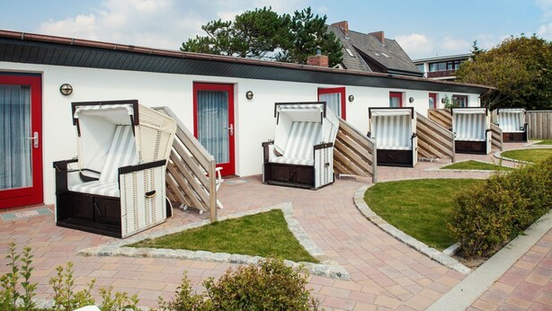 A row of outdoor lounge chairs and a building with red doors and a white exterior.