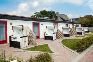 A row of outdoor lounge chairs and a building with red doors and a white exterior. - Riterspöör - House Ilse - Apartment Riterspöör (Sylt)