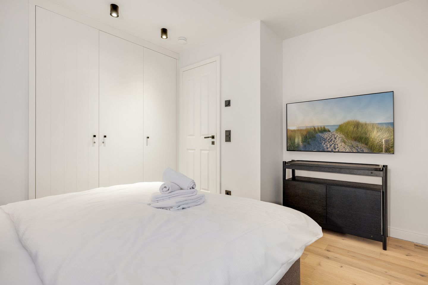 A bedroom with a bed, white wardrobe, and a painting on the wall.