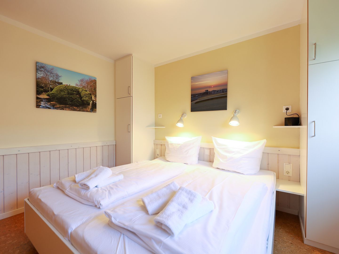 Une chambre d’hôtel avec un lit, deux lampes de chevet, un tableau au mur et une armoire.