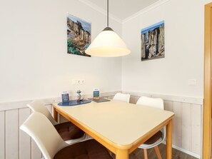 Een eetgedeelte met een tafel en stoelen, twee aan de muur bevestigde schilderijen, een hanglamp en een klein decoratief object op de tafel.