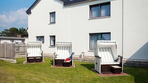 A two-story building with a white exterior and multiple windows. There are three outdoor lounge chairs with striped cushions. - Imke - House Rolf - Imke (Sylt)