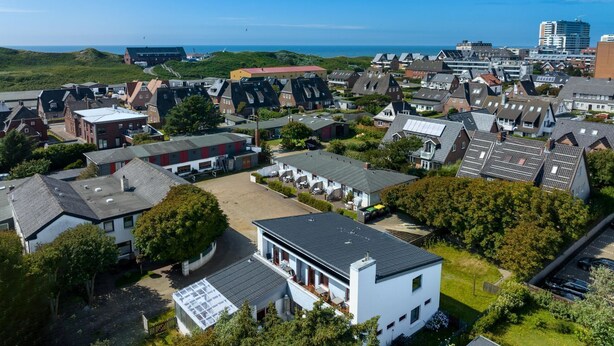 An aerial view of a residential area with houses, a parking lot, and a view of the sea. - Imke - House Rolf - Imke (Sylt)