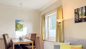 A cozy room with a wooden dining table, chairs, a sofa, and a window with curtains. - Imke - House Rolf - Imke (Sylt)