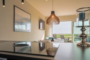 Uma sala de jantar moderna com mesa de vidro, cadeiras e luminária pendente.