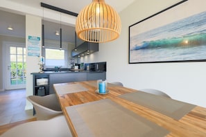 Uma cozinha moderna com uma mesa de jantar de madeira, um lustre e uma pintura emoldurada de uma onda do mar.