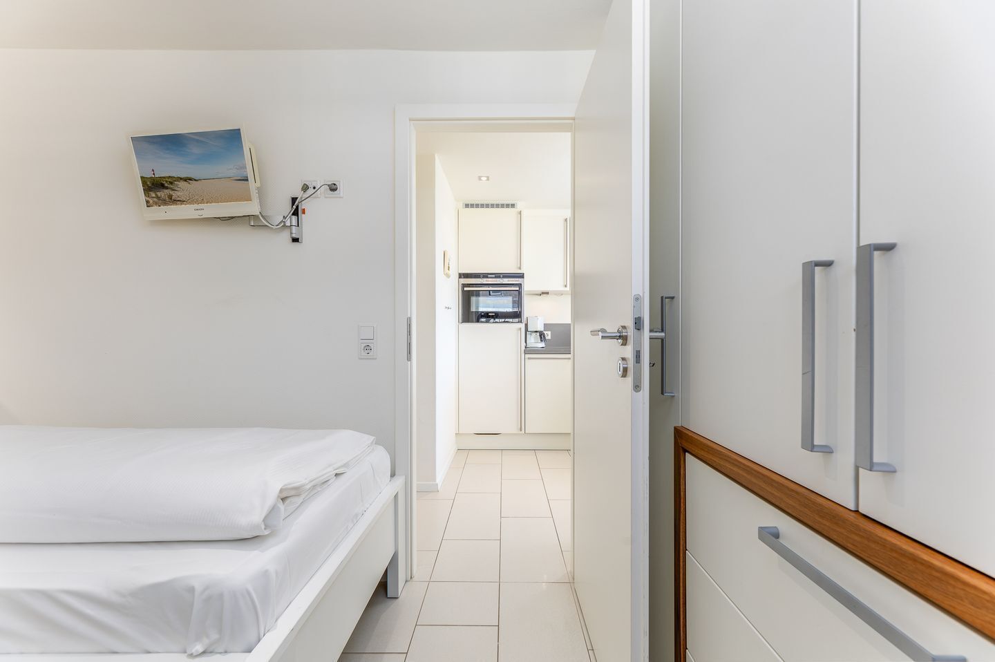 A hotel room with a bed, a kitchenette, and a bathroom visible through an open door.