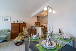 Un moderno comedor con una mesa de vidrio dispuesta para dos personas, una silla de mimbre y un tapete verde.
