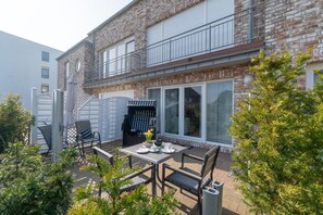 Una casa de ladrillo de dos pisos, con un balcón, un patio con mobiliario exterior y una zona de estar cubierta.