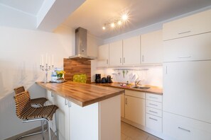 Una cocina moderna con armarios blancos, una encimera de madera y una estufa integrada. Hay dos taburetes de bar y un jarrón con flores sobre la encimera.